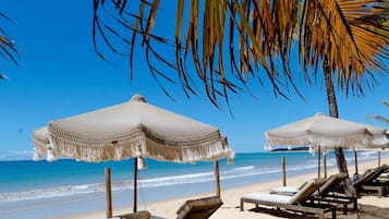 A beach with thatched umbrellas and lounge chairs.