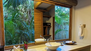 Un baño con un amplio ventanal, un lavabo blanco y un mueble de tocador de madera.