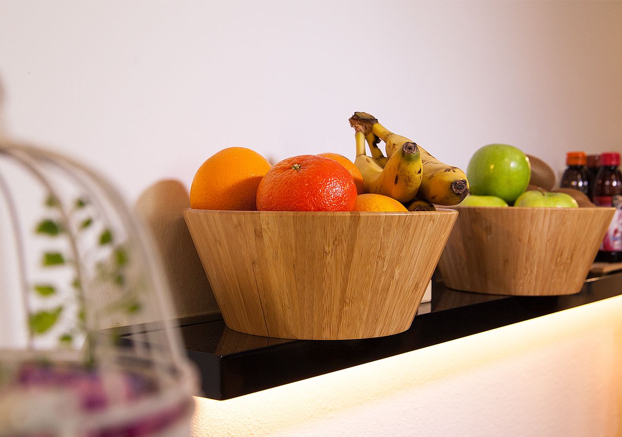 Dos cuencos de madera sobre una encimera, uno con naranjas y plátanos, y el otro con manzanas.