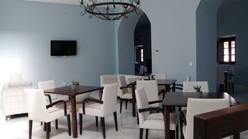 A dining area with a large table and chairs, a chandelier, and a TV mounted on the wall.