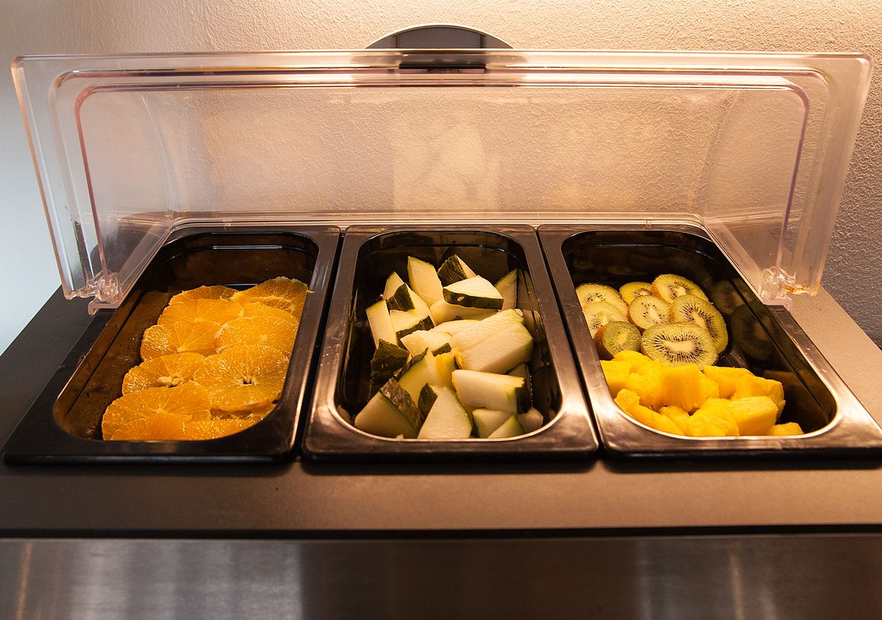 A buffet with three trays containing sliced oranges, cheese, and kiwi.
