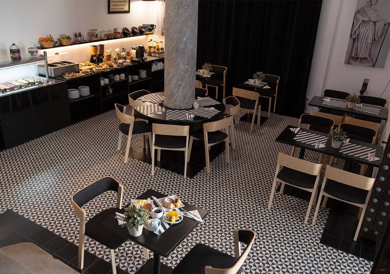 Un restaurant dont le sol est recouvert de carreaux noirs et blancs, avec des tables rondes surmontées de sets de table à rayures, et où une grande variété de plats et de boissons sont exposés.
