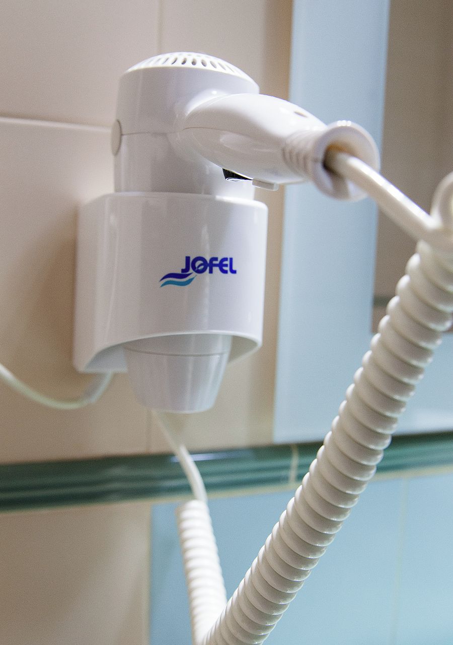 Un dispositivo JOFEL blanco sujeto a una pared con un cable flexible blanco.