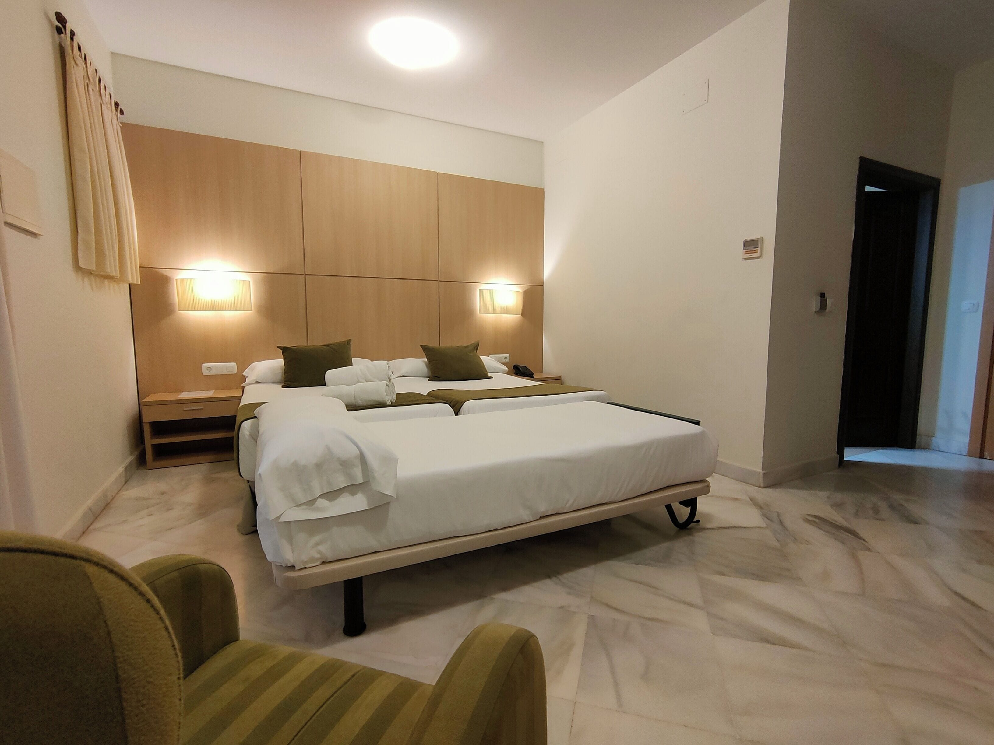 A hotel room with a large bed, bedside tables, and a headboard with integrated lighting.