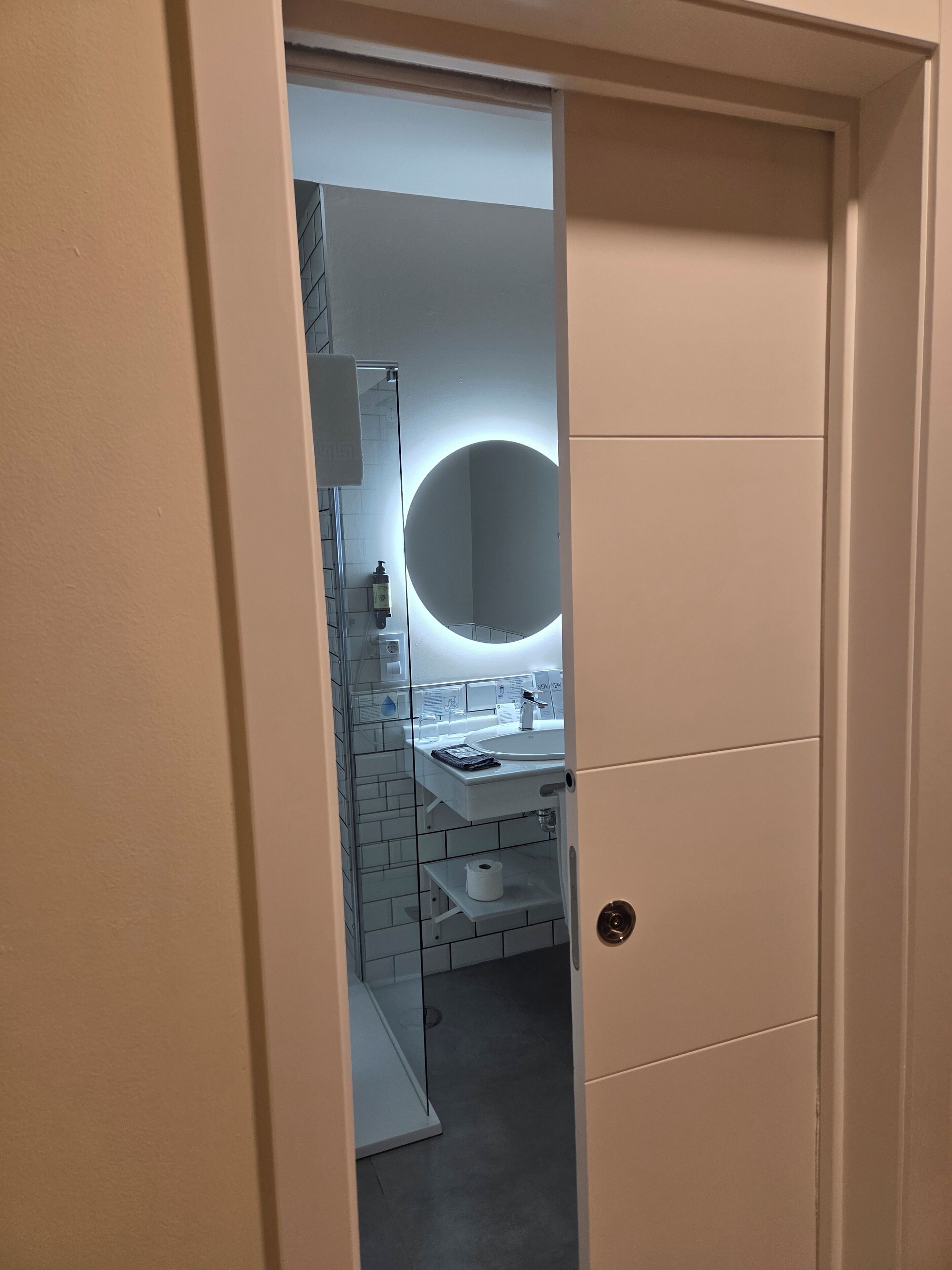 Un baño moderno con cabina de ducha de vidrio, un espejo redondo y un lavamanos blanco.