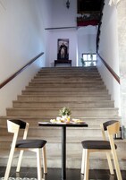 Una escalera con una mesa y sillas al frente, que lleva a un cuarto con un cuadro en la pared.