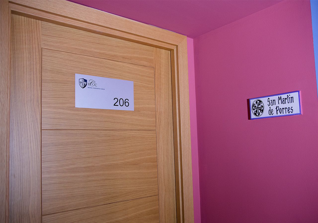 A hotel room with a wooden door labeled "206" and a sign on the wall reading "San Martin de Porres."