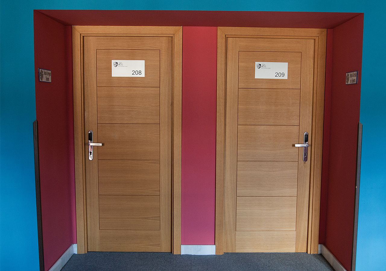 Deux portes en bois, portant les numéros « 208 » et « 209 », se trouvent dans un couloir aux murs rouges, dont l’un est peint en bleu pour créer un effet de contraste.