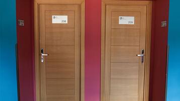 Deux portes en bois, portant les numéros « 208 » et « 209 », se trouvent dans un couloir aux murs rouges, dont l’un est peint en bleu pour créer un effet de contraste.