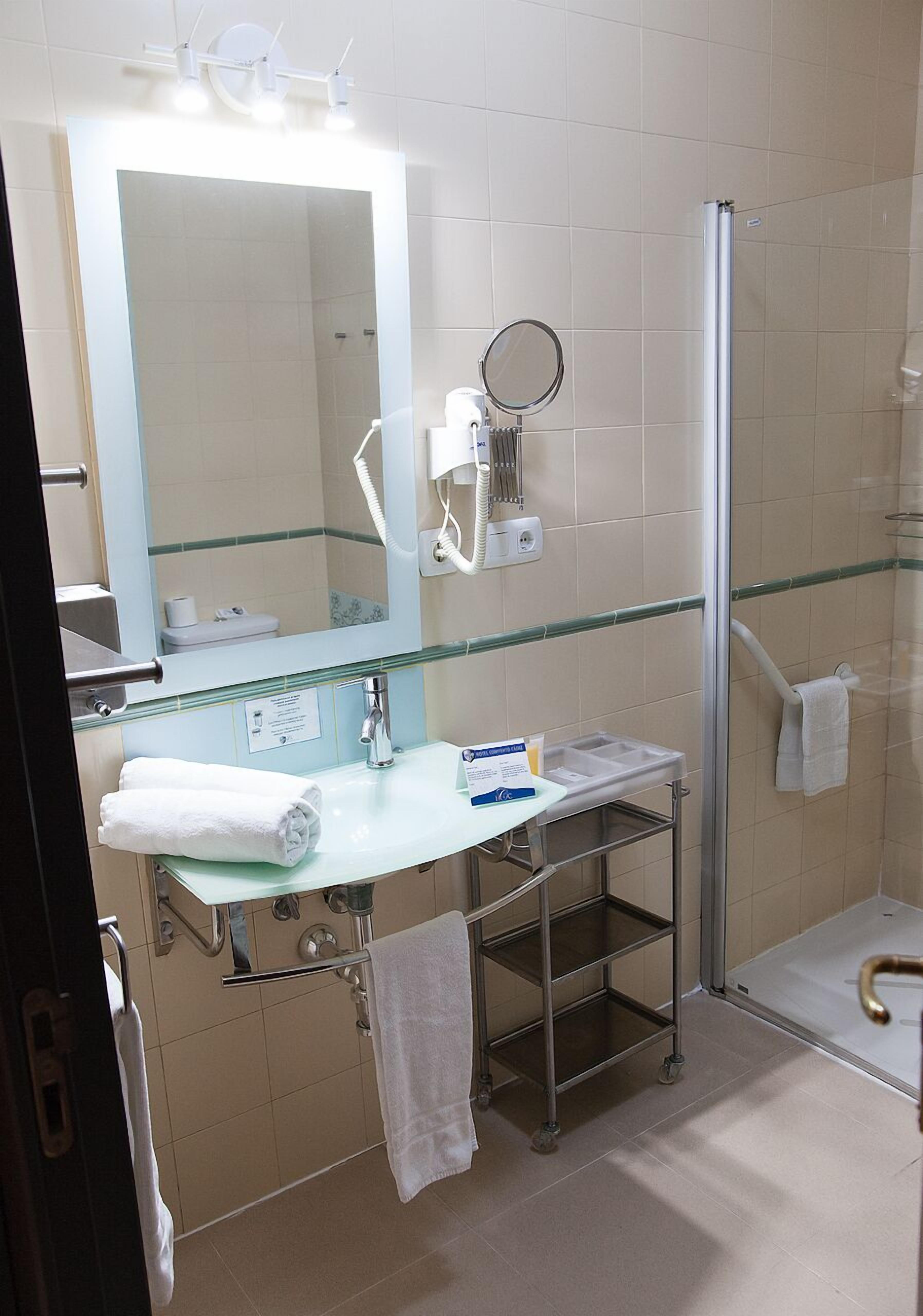 Un baño moderno con cabina de ducha de vidrio, un lavabo blanco con espejo y un perchero para toallas.