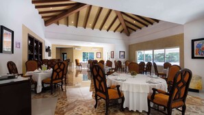 A spacious dining area with multiple tables and chairs, a high ceiling with wooden beams, and large windows providing natural light. - MM Grand Hotel Puebla, Tapestry Collection by Hilton (Puebla)