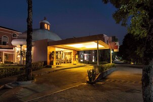 Entrada de hotel con un espacio exterior cubierto, un edificio con forma de cúpula y una bandera.