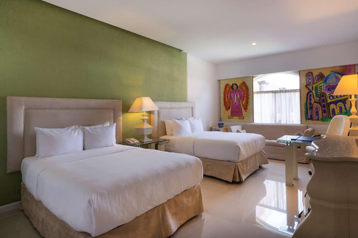 A hotel room with two beds, a desk, a chair, and artwork on the walls.