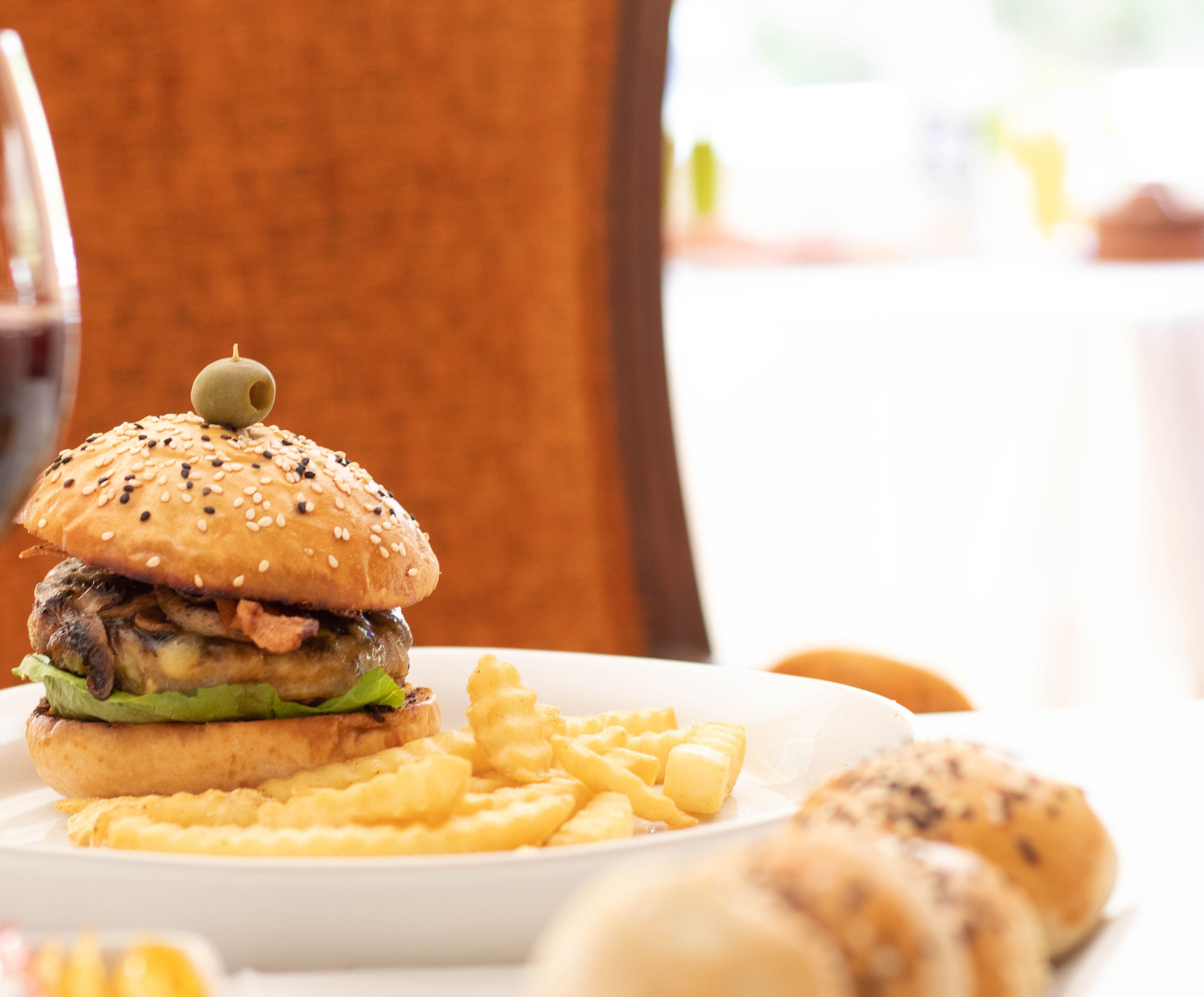 Comida que incluye una hamburguesa con pan de sésamo y una porción de papas fritas, sobre un plato blanco.