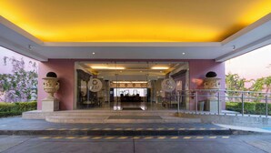 A hotel entrance with a glass facade, a reception desk, and a staircase leading up to the lobby. - MM Grand Hotel Puebla, Tapestry Collection by Hilton (Puebla)