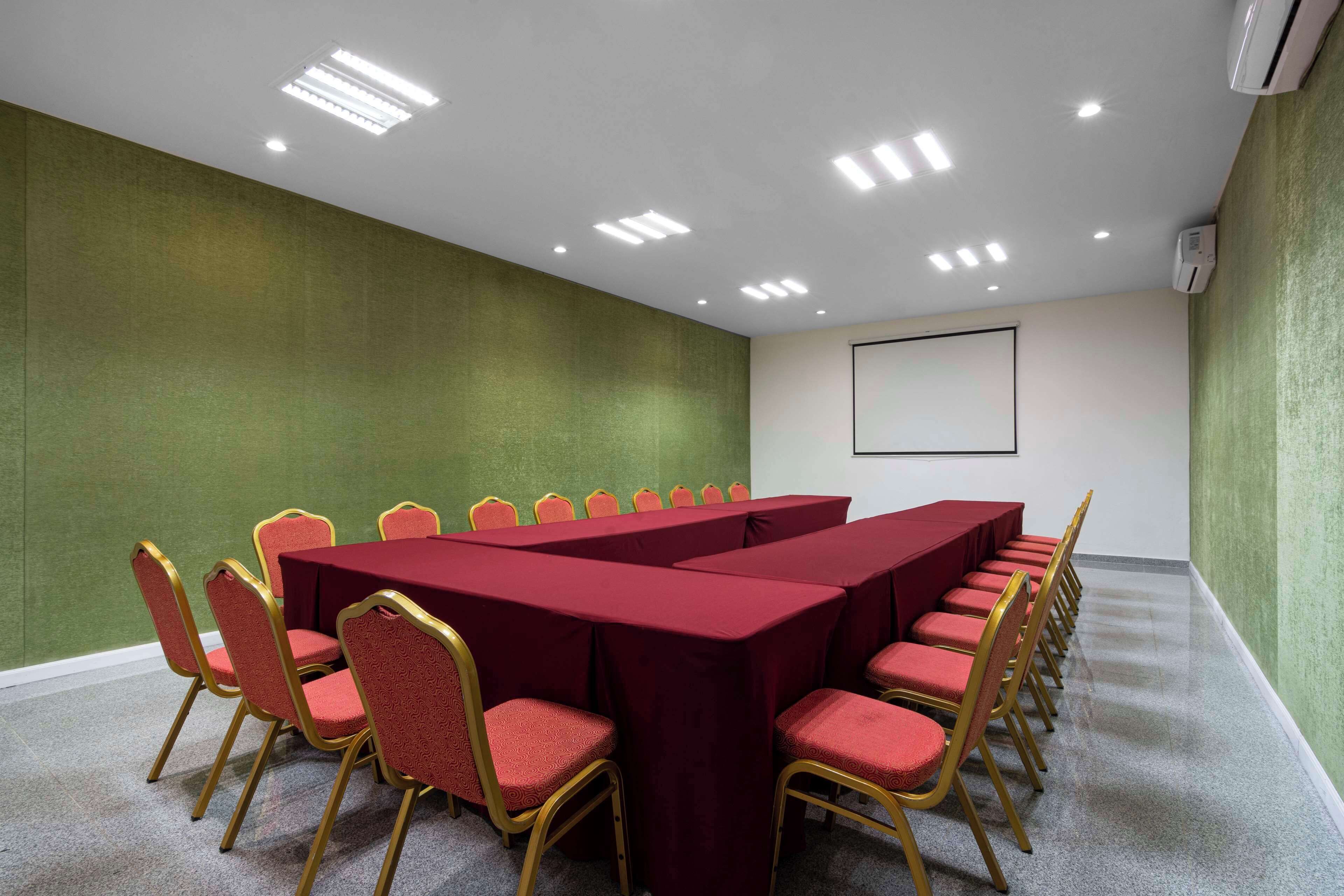 A conference room with a long table, red chairs, and a projector screen.