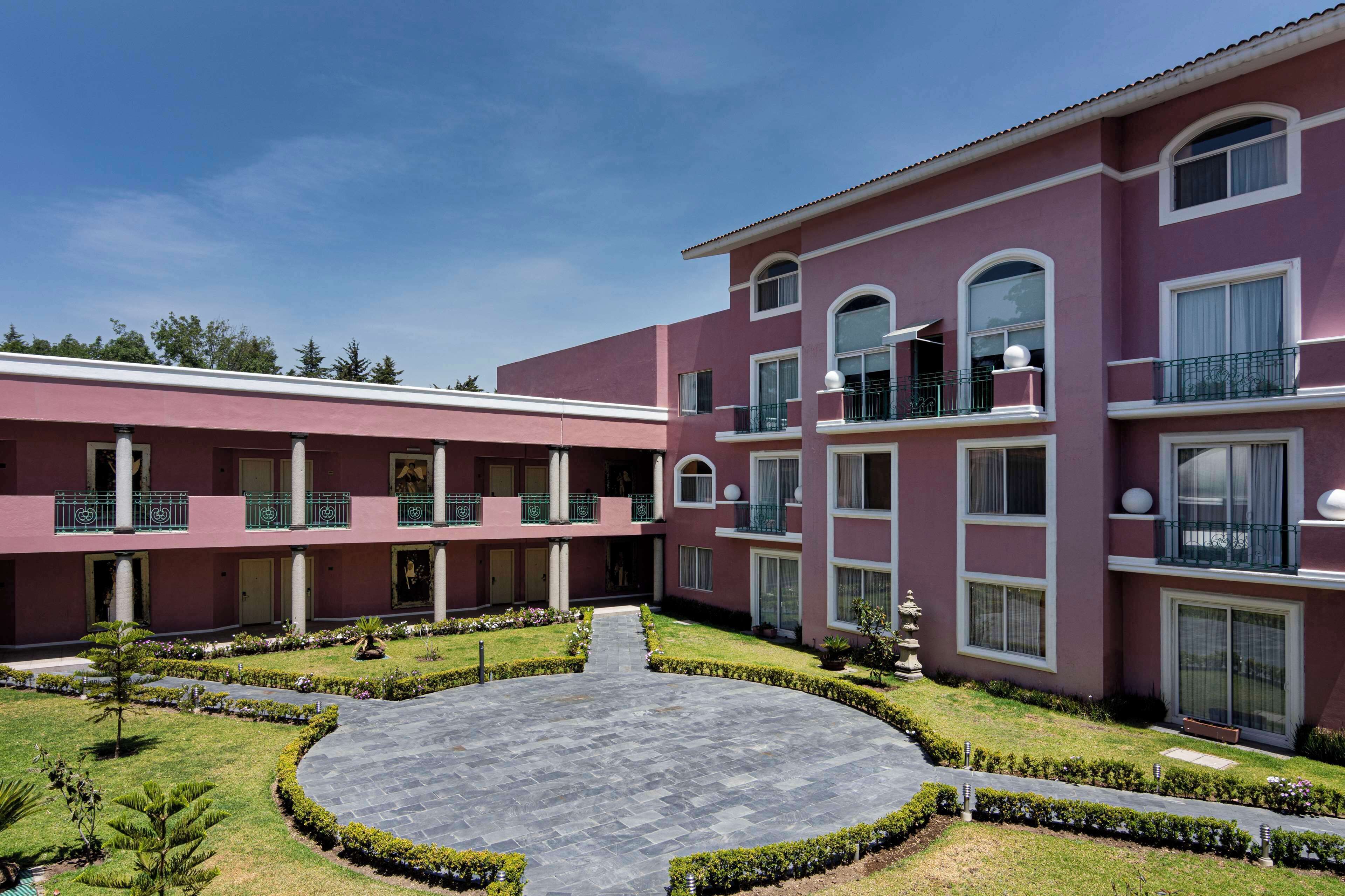 Un hotel de varios pisos con un patio central, balcones y un jardín bien cuidado.