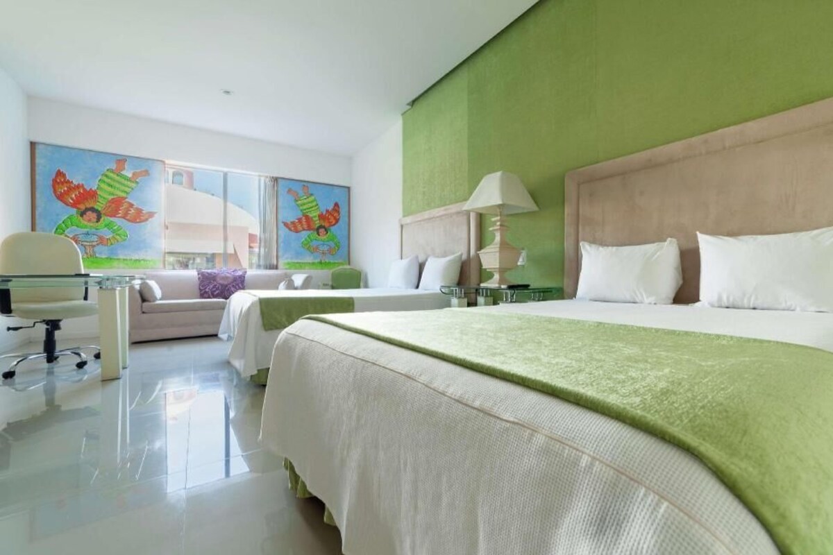 A hotel room with a large bed, a smaller bed, a desk, a chair, and a painting on the wall.