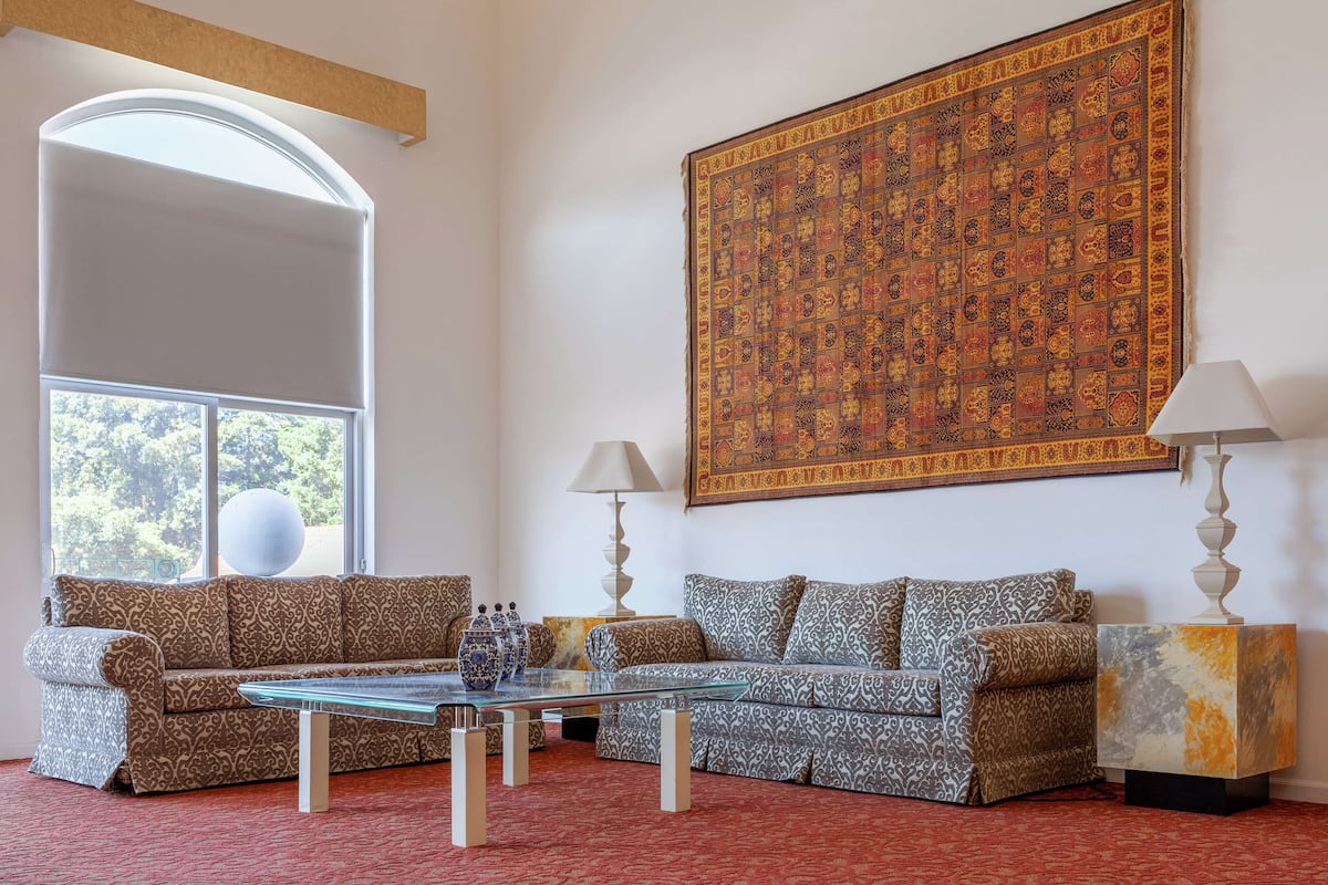A living room with two sofas, a glass coffee table, and a large patterned tapestry on the wall.
