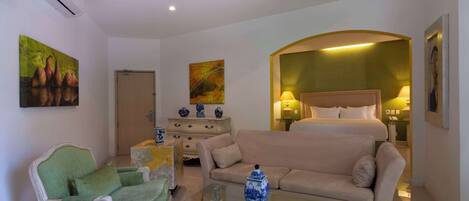 A modern hotel room with a bed, a sofa, a chair, and a glass coffee table.