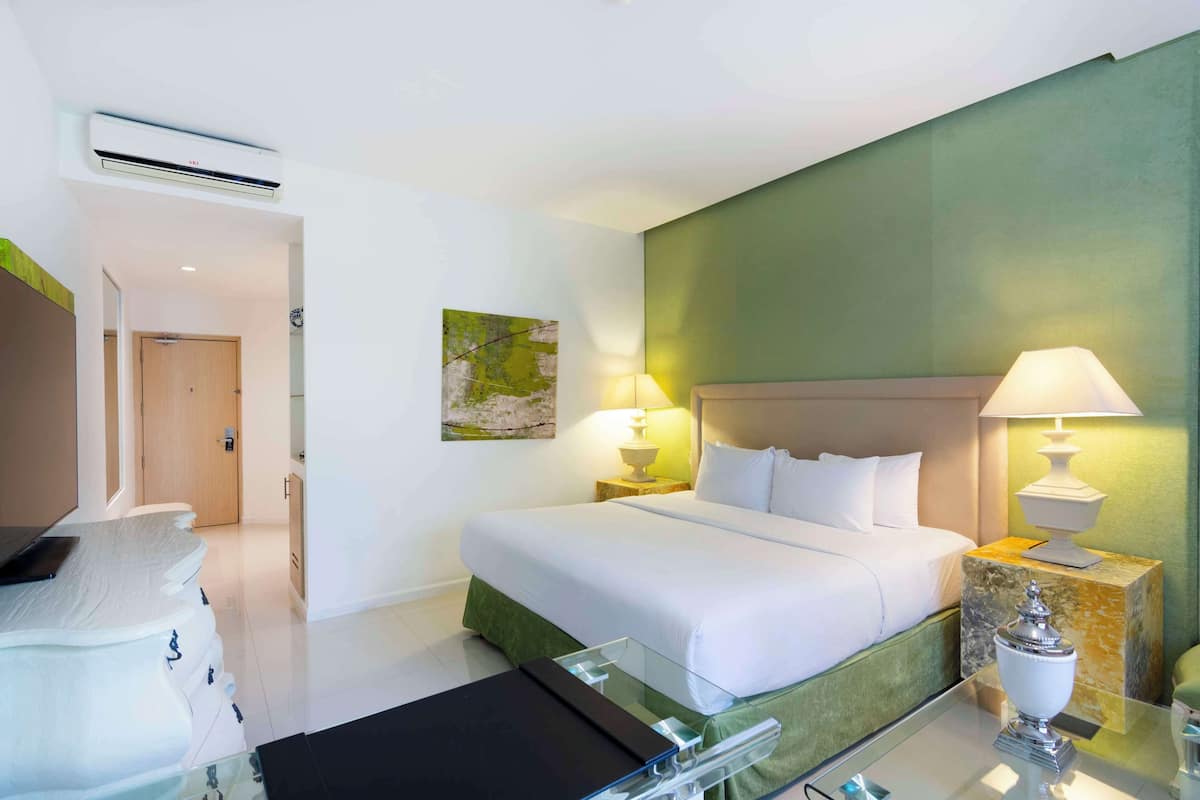 A hotel room with a bed, bedside tables, a glass coffee table, a wall-mounted air conditioner, and a green accent wall.