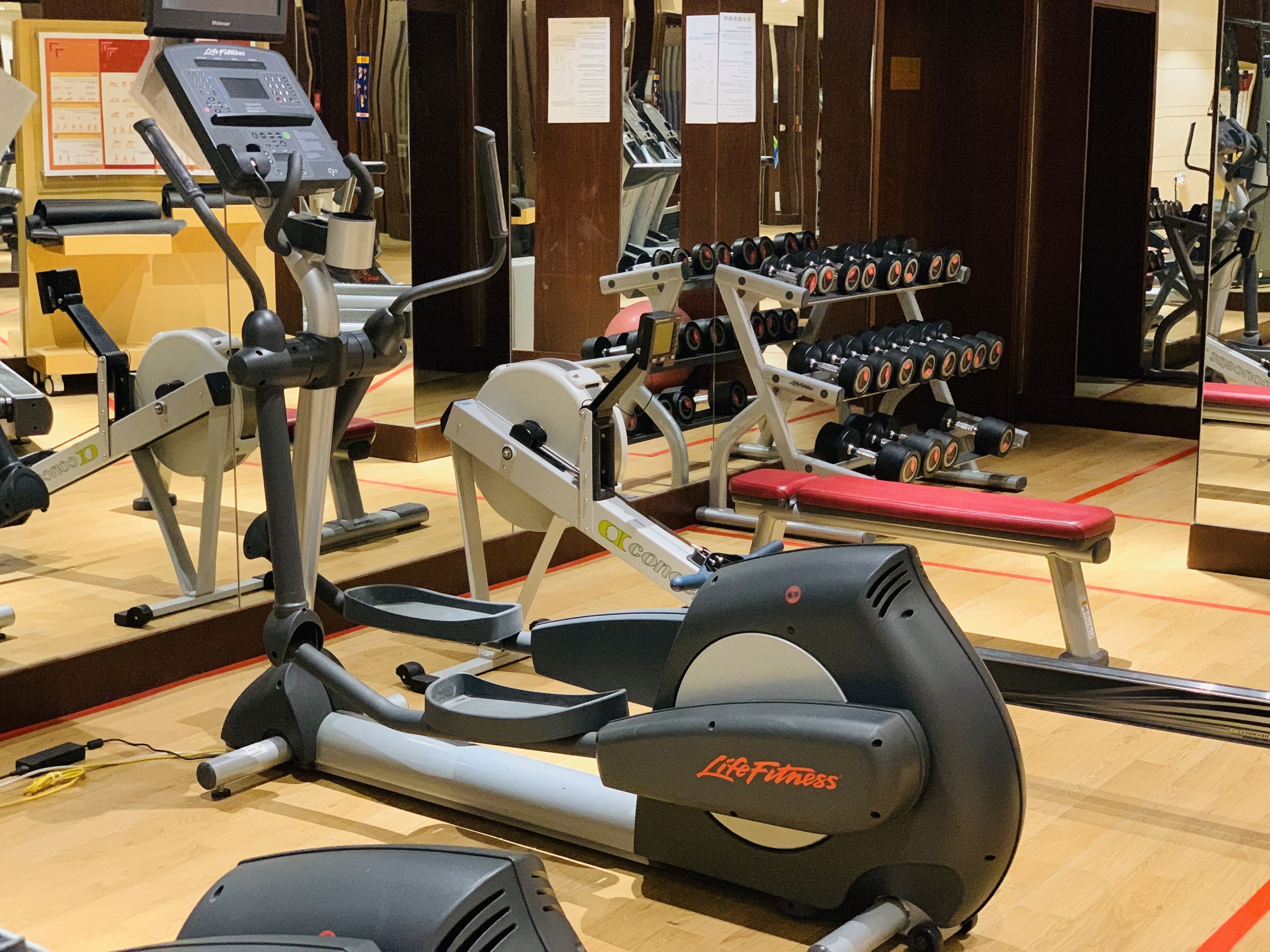Una palestra con diverse attrezzature per l'allenamento, tra cui tapis roulant, macchinari per pesi e manubri.