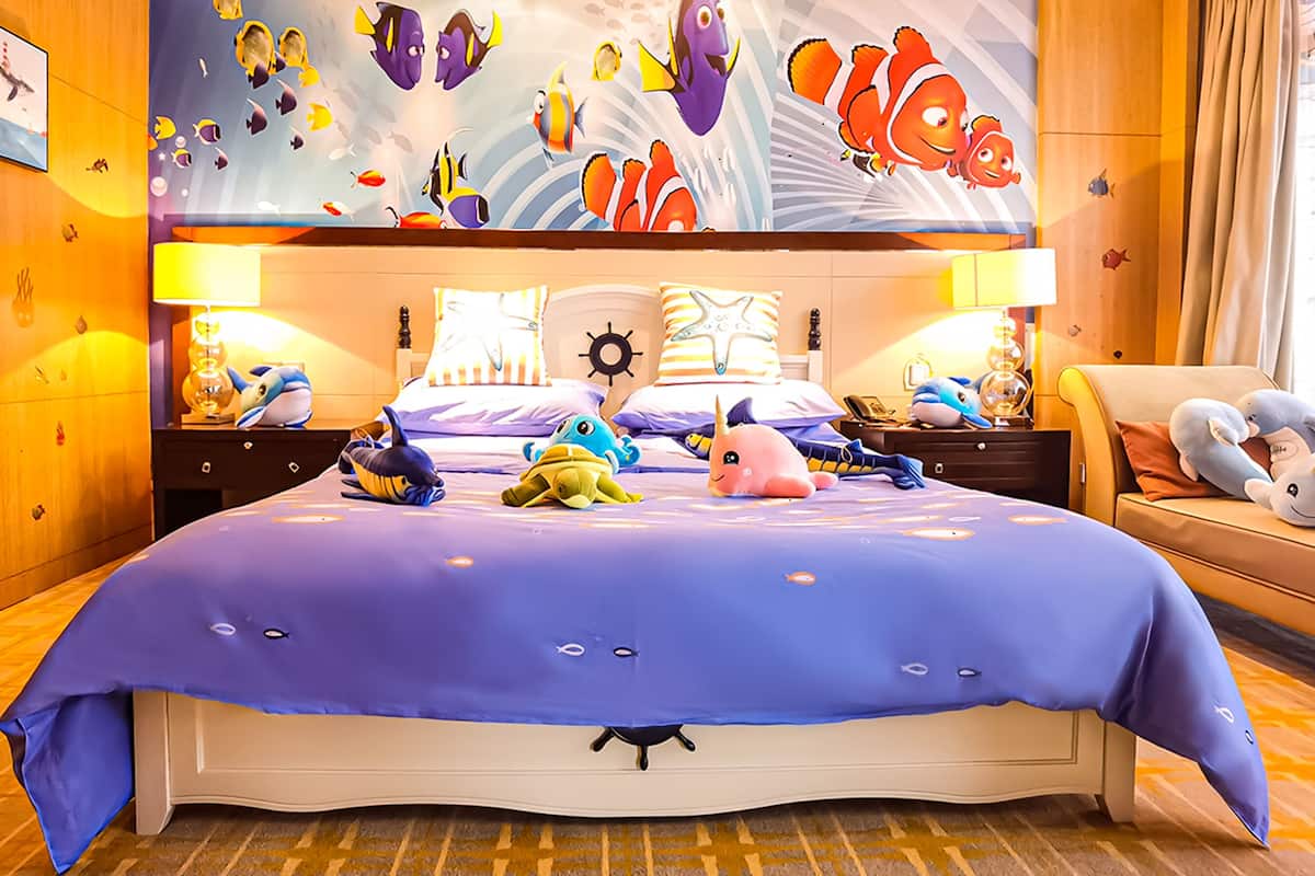 Une chambre d’hôtel avec un grand lit, des peluches et une fresque représentant des poissons sur le mur.