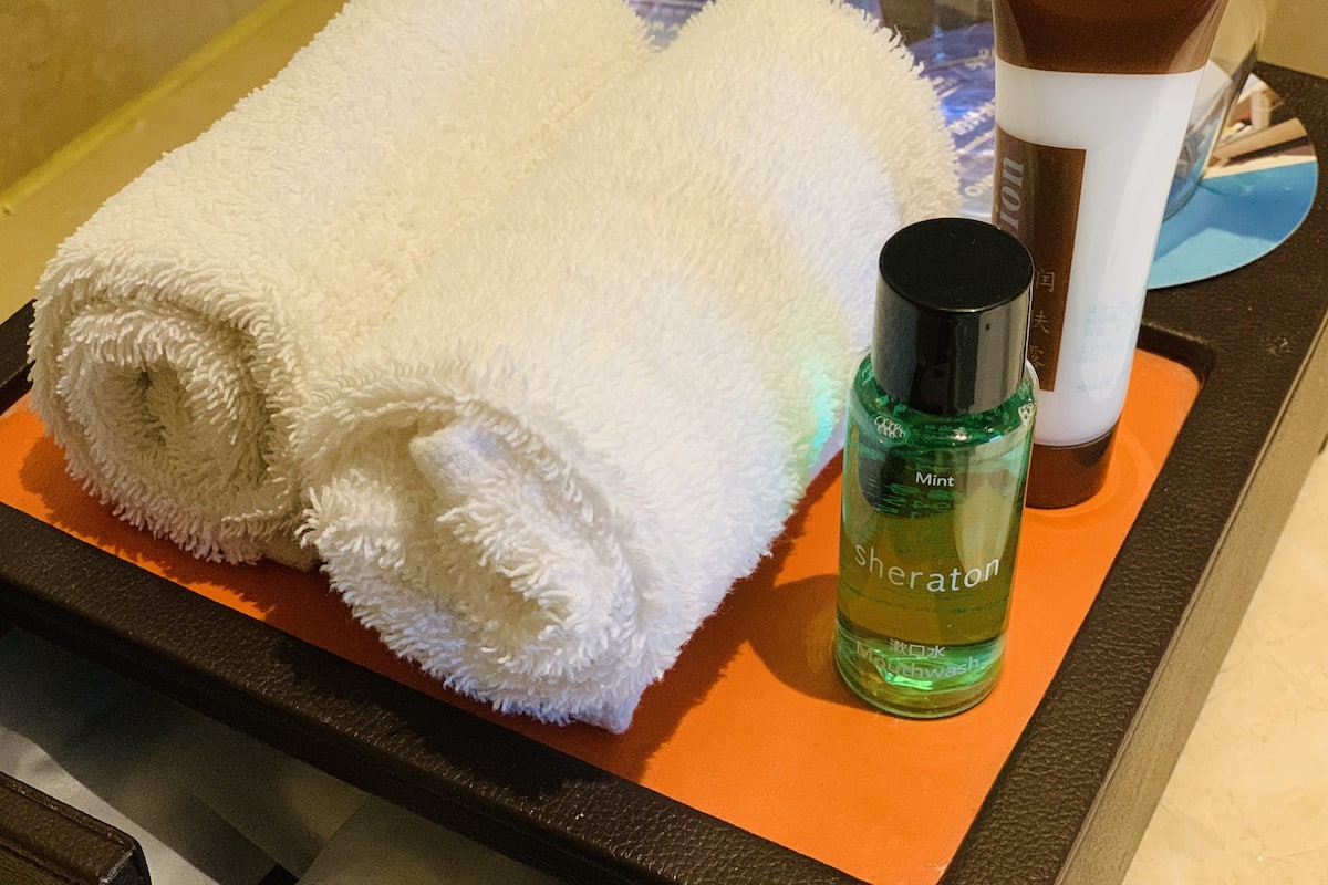 Une serviette blanche roulée et une bouteille de bain de bouche Sheraton, le tout posé sur un plateau.