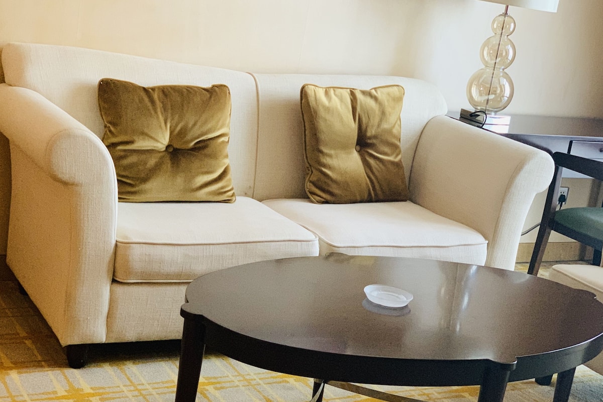 Un salon avec un canapé, deux coussins dorés, une petite table ronde et une lampe.