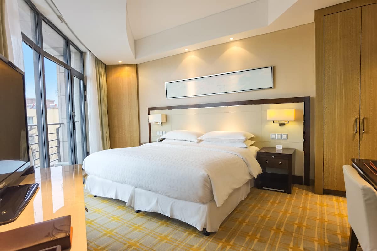 Une chambre d’hôtel avec un grand lit, un bureau avec un ordinateur portable, une table de chevet et une armoire.