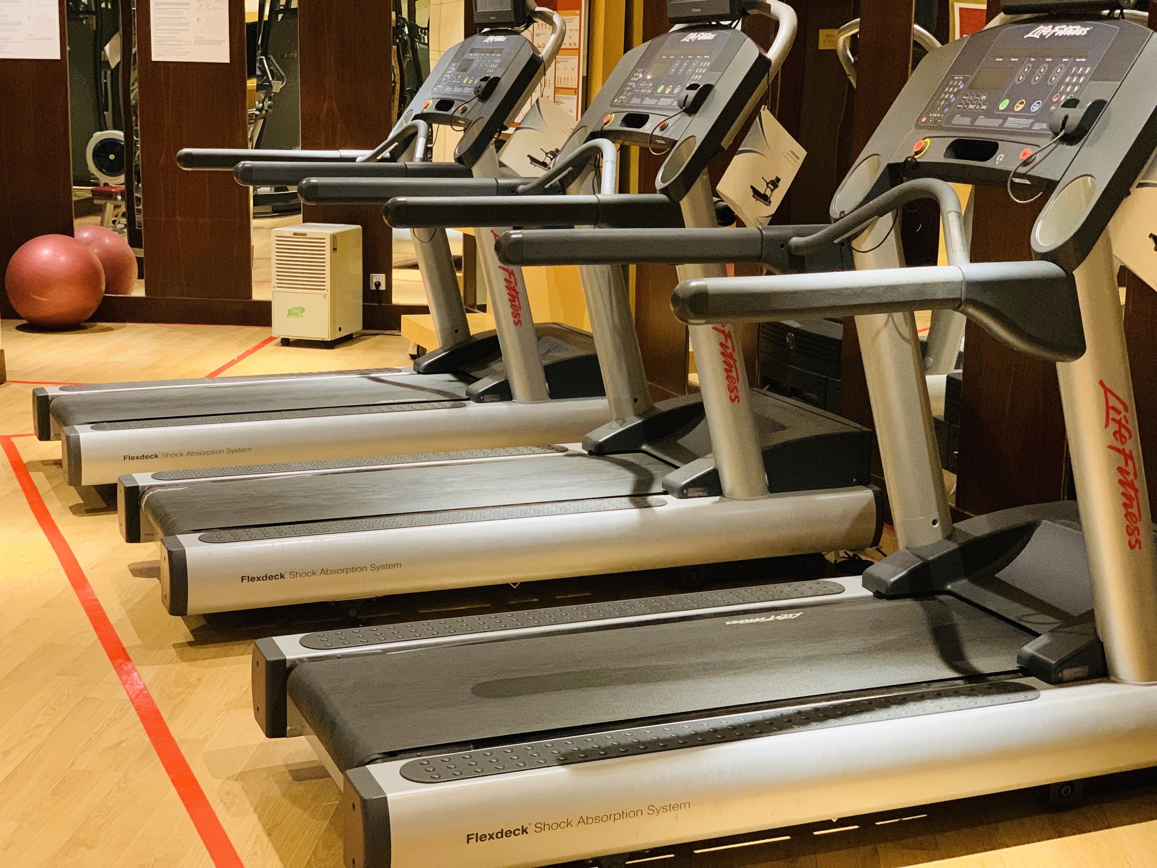 A row of treadmills with FlexDeck Shock Absorption System, in a gym with wooden flooring and exercise balls in the background.