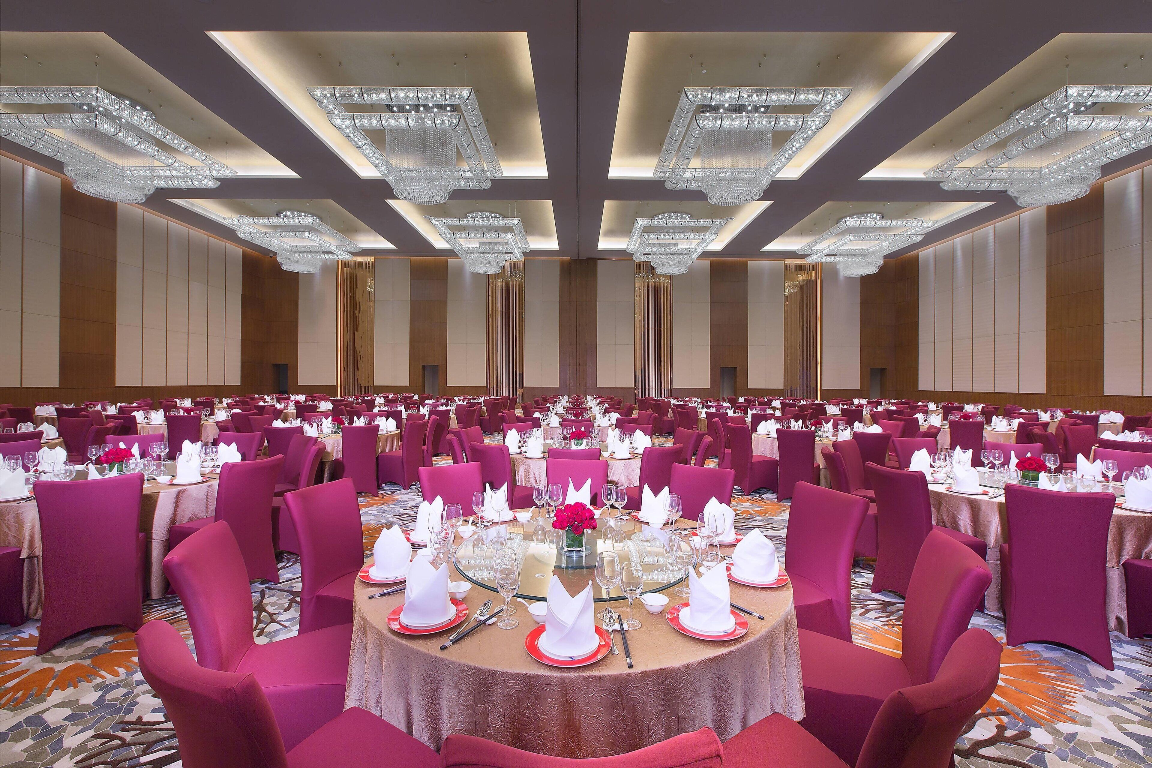 A banquet hall with round tables set for dining, featuring pink chairs and white table settings.