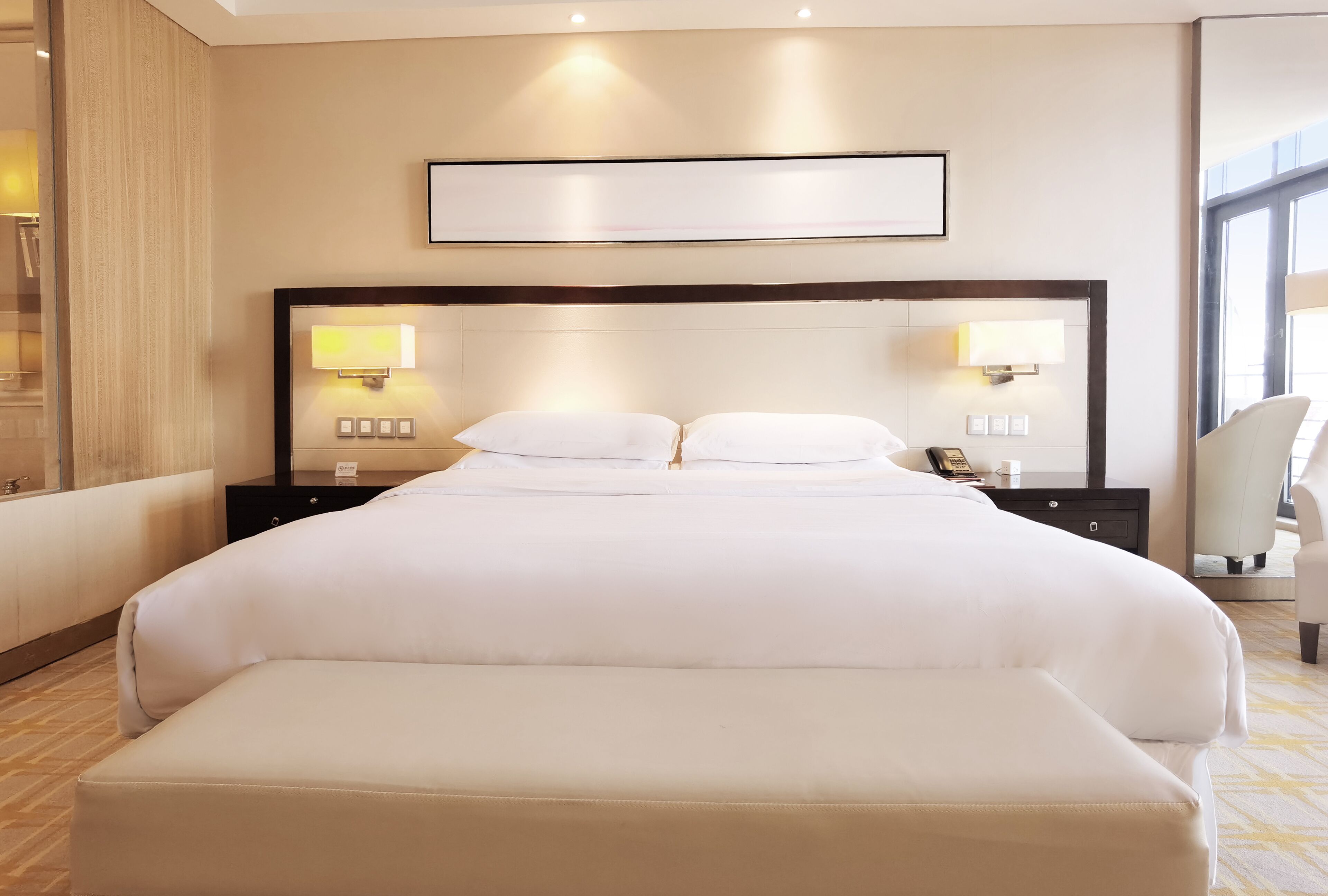 Et hotelværelse med en stor seng, to sengeborde med lamper, en stol og et stort vindue.