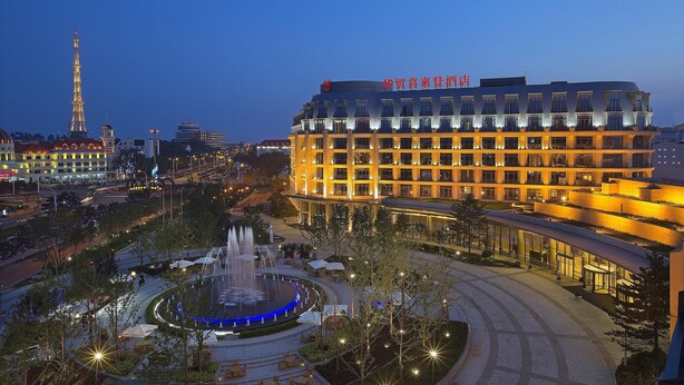 A hotel with a modern design, featuring a large central courtyard with a fountain, surrounded by trees and outdoor seating areas. - Sheraton Qinhuangdao Beidaihe Hotel (Qinhuangdao)