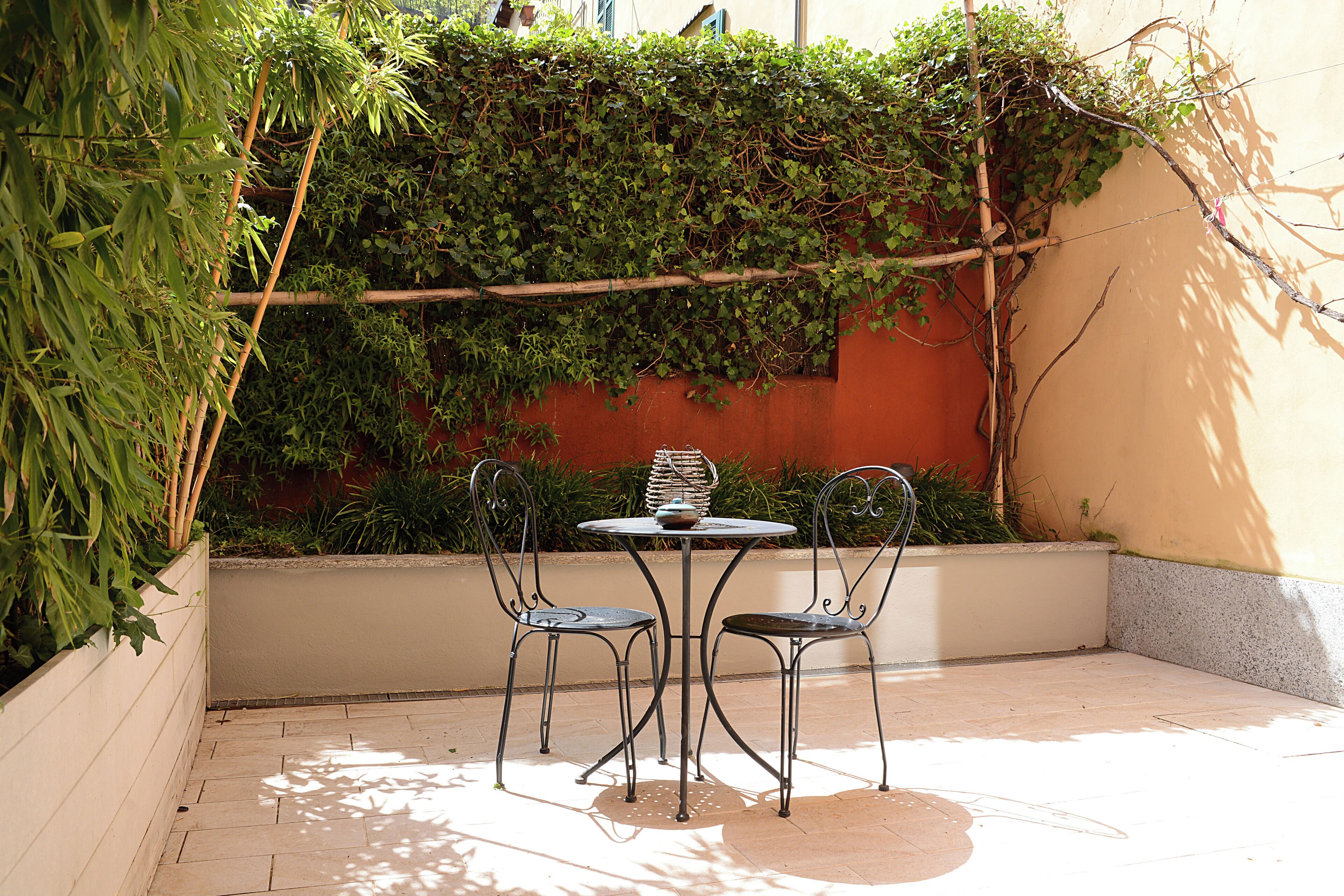A patio with a table and two chairs, surrounded by a wall covered in greenery.
