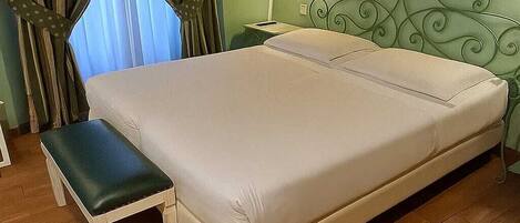 Une chambre à coucher avec un grand lit, un banc, une table de chevet et une lampe fixée au mur.