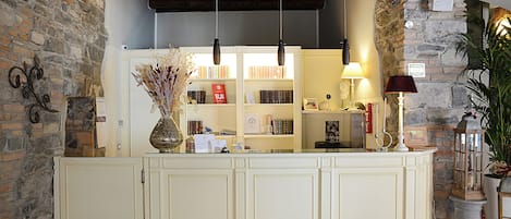 A reception desk with a stone wall backdrop, a bookshelf, and a vase with dried flowers.