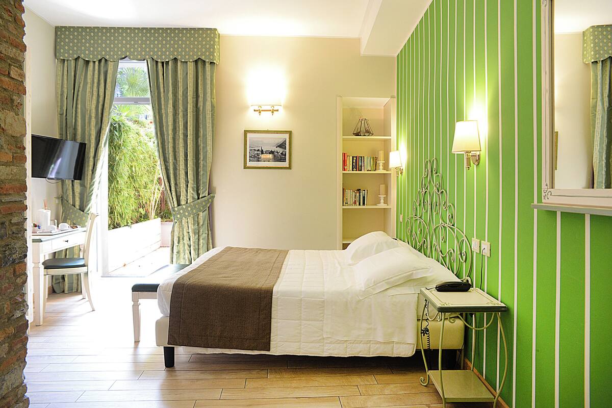Un dormitorio con cama, mesita de noche, lámpara, estantería y televisor sobre un mueble.