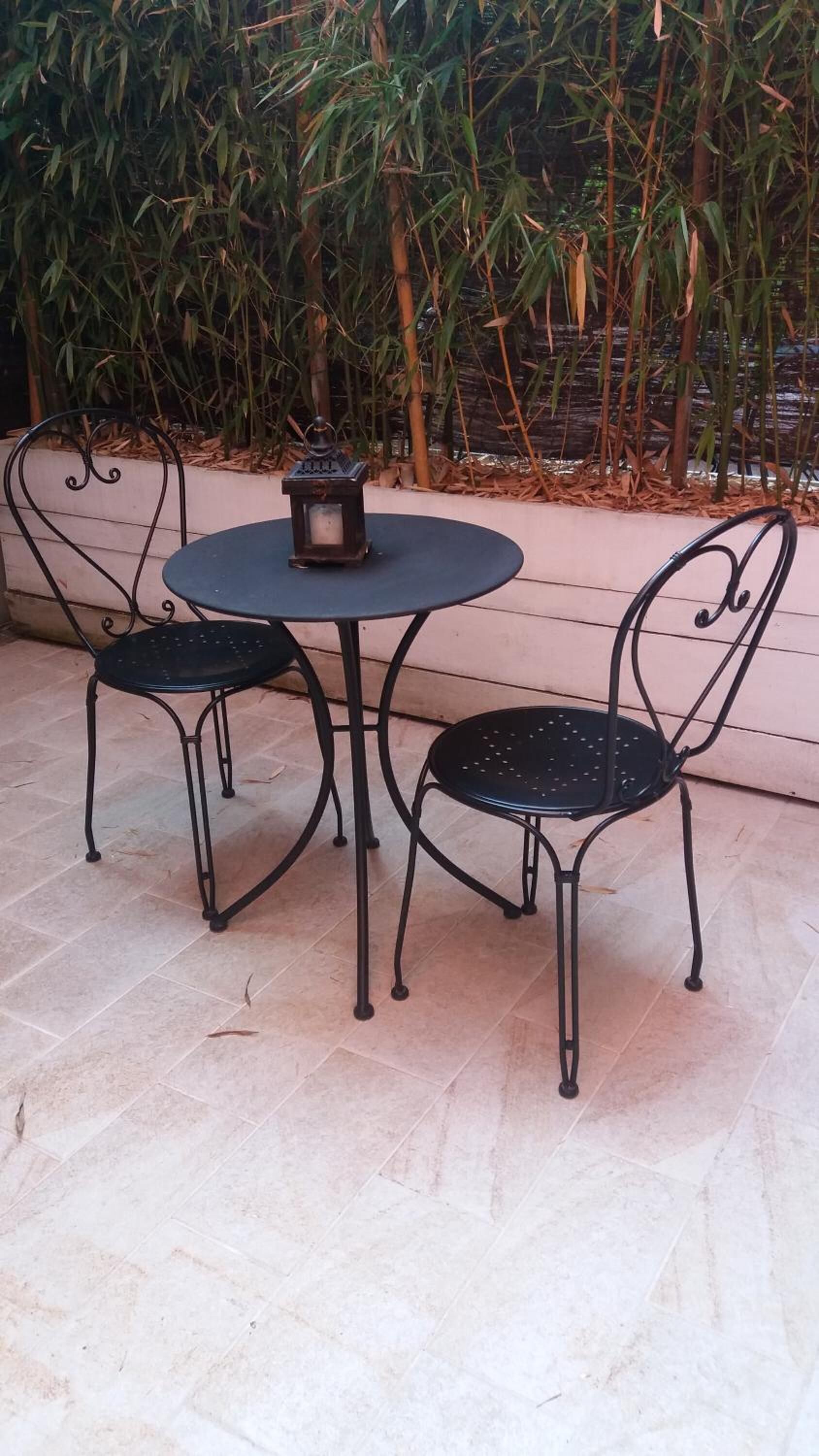 A round table with two chairs, a lantern, and a bamboo backdrop.