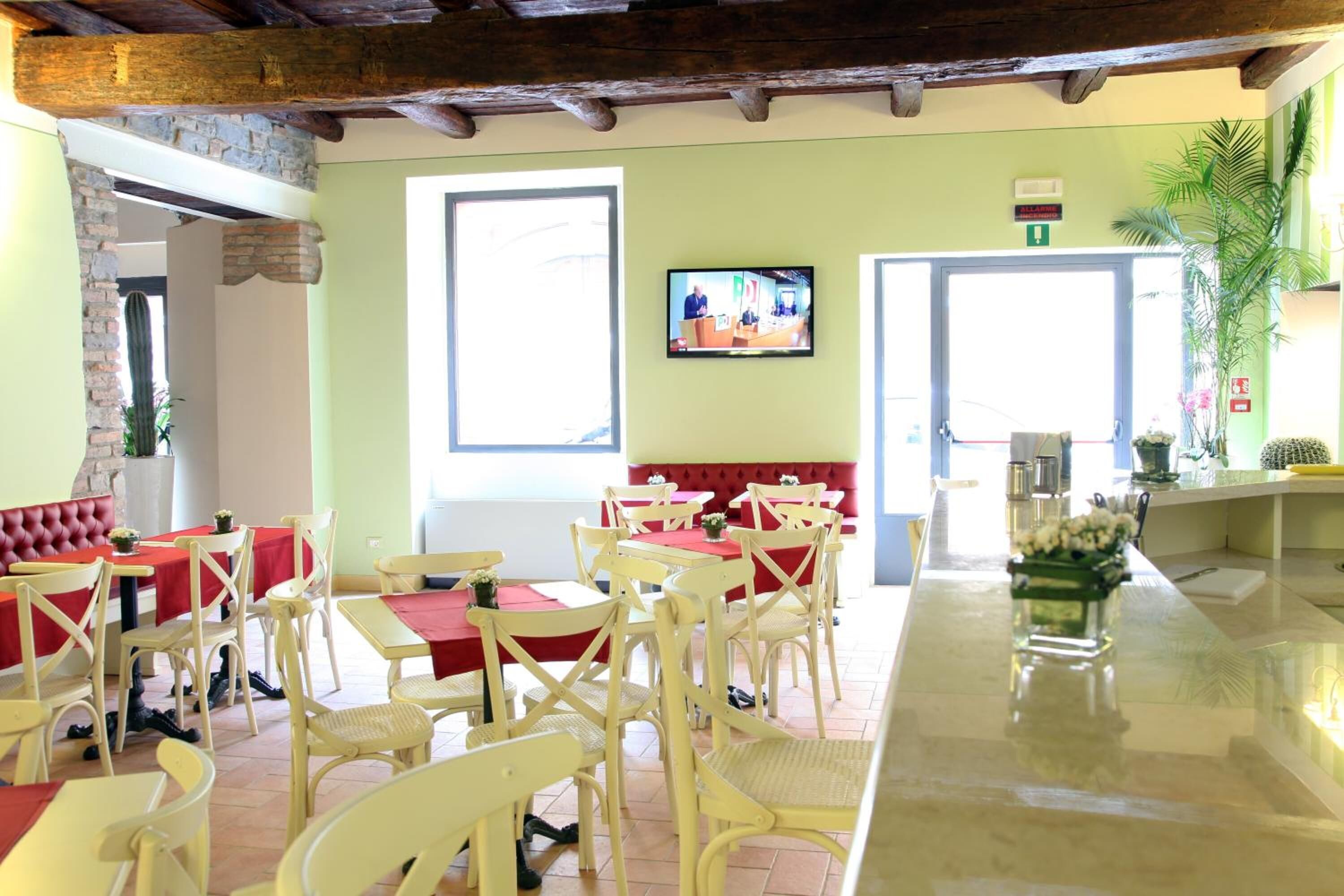 A restaurant with yellow chairs and red tablecloths, a television on the wall, and a cactus in the corner.