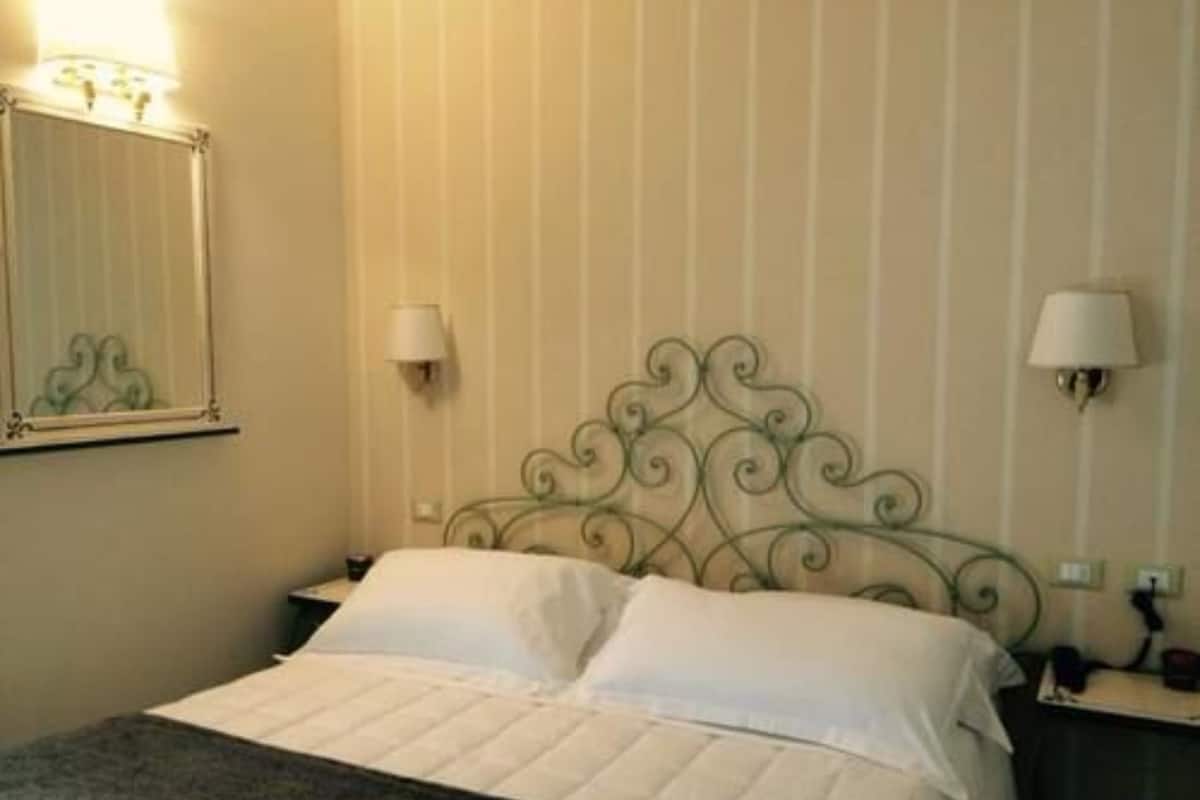 Una cama bien hecha con colcha blanca, un cabecero metálico decorativo y dos lámparas de noche.
