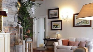 Un salon avec un canapé blanc, une table basse, un tapis à motifs, un mur en pierre et une porte.