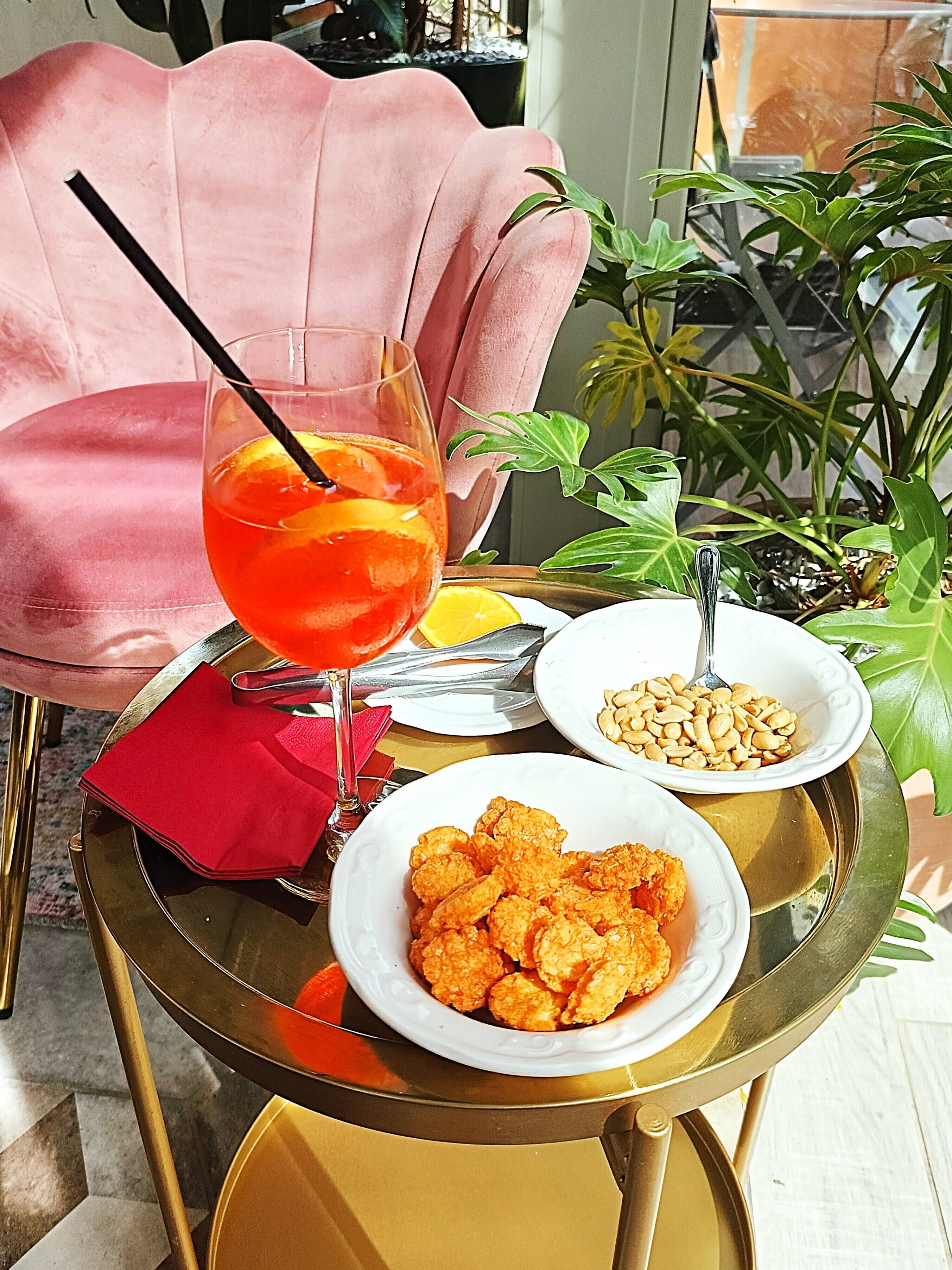 A table with a glass of orange drink, a plate of snacks, and a small bowl of nuts.