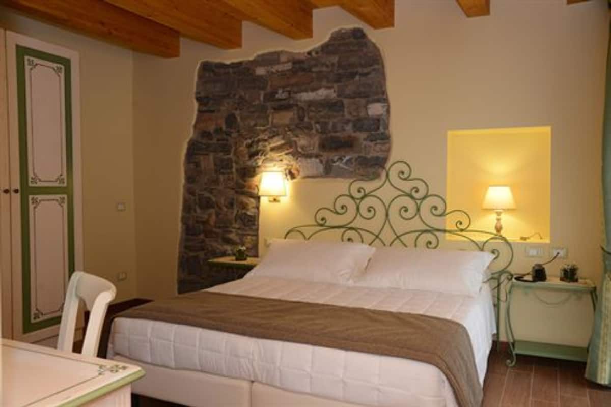 Un dormitorio con pared de piedra, una cama con ropa de cama blanca, dos lámparas de noche y una silla.