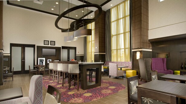 Un hall d’hôtel doté d’un bar, de différents espaces pour s’asseoir et de grandes fenêtres laissant entrer la lumière naturelle.