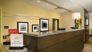 Un comptoir d’accueil d’hôtel avec une pancarte « Bienvenue à Buffalo », des photos encadrées accrochées au mur et une pancarte « Hilton Honors ».