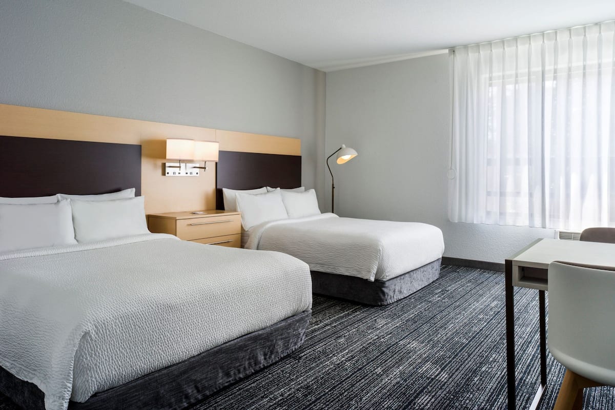 Een hotelkamer met twee bedden, een bureau, een stoel, een lamp en een raam met gordijnen.