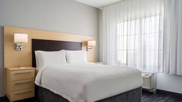 A hotel room with a bed, two bedside tables, a nightstand, a window with curtains, and a carpeted floor.