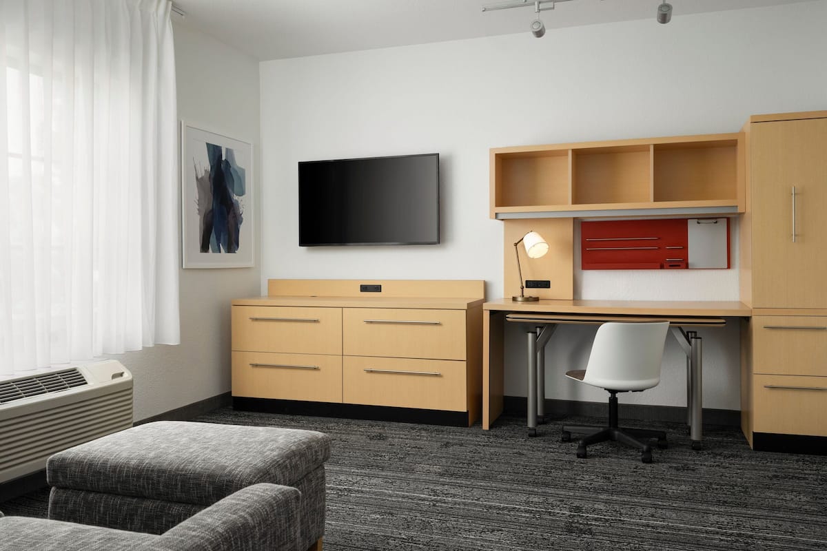 Een moderne hotelkamer met een flatscreen-tv, een bureau met stoel, een kledingkast en een groot raam met gordijnen.