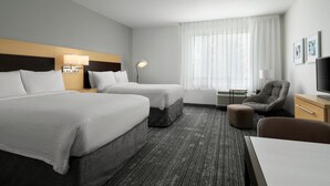 Une chambre d’hôtel avec deux lits, un bureau, une chaise, une télévision et une fenêtre avec des rideaux.